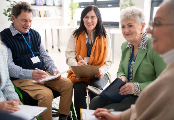istock Excited elderly people attending group therapy session at nursing house, positive senior man and woman sitting in circle, having conversation with psychologist 1407578355