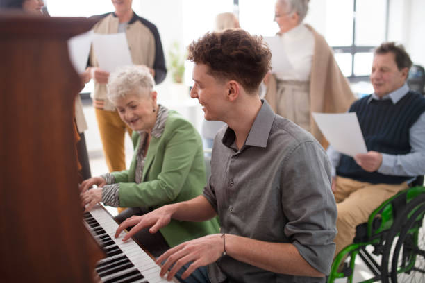 聖歌隊のリハーサルでピアノを弾く若い先生を持つ年配の女性。 - リタイアメントコミュニティ ストックフォトと画像