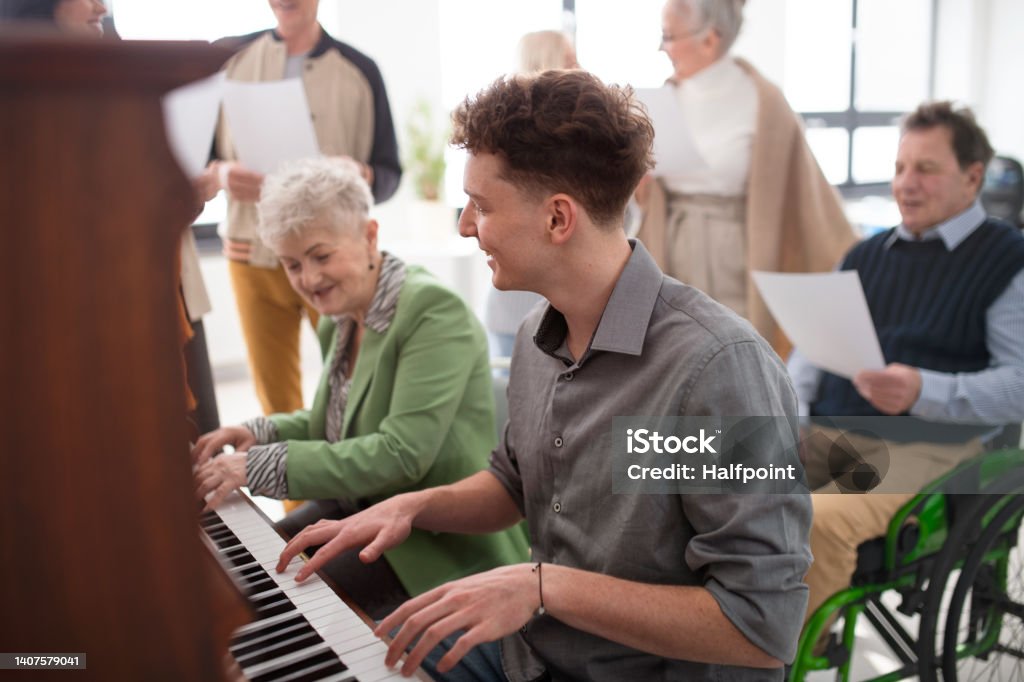 Senior woman with young teacher playing at piano in choir rehearsal. A senior woman with young teacher playing at piano in choir rehearsal. Nursing Home Stock Photo