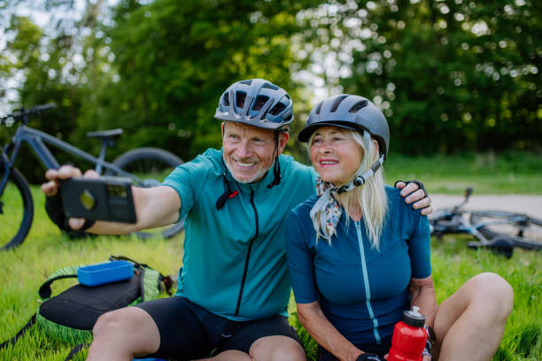 istock Active senior couple resting after bicycle ride at summer park, sitting on grass and taking slefie. 1407580311