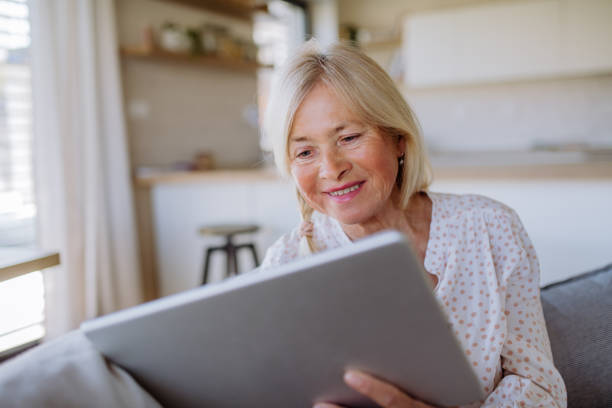 istock Senior woman sitting on sofa and rusing tablet at home 1407581549