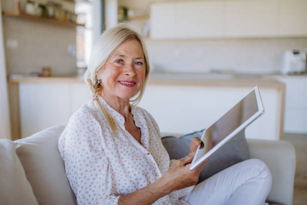 istock Senior woman sitting on sofa and rusing tablet at home 1407581568