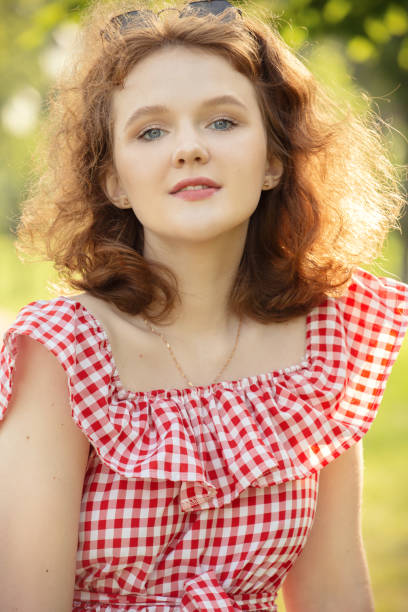 beautiful girl with bare shoulders dress and curly red hair looking at camera in sun light