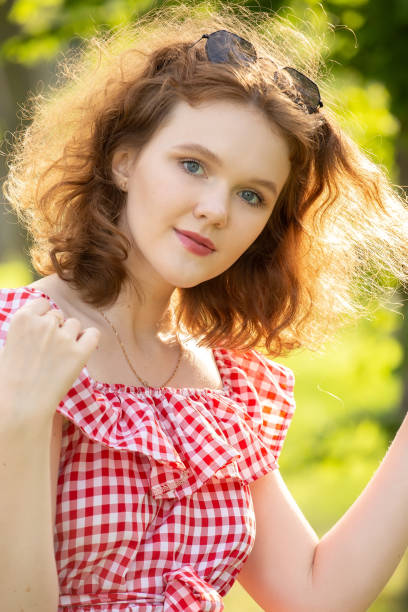beautiful girl with red dress and curly red hair looking at camera in sun light