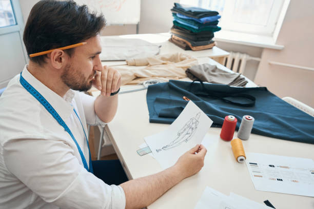 istock Man couturier sits at desk with sketch in hands 1407590462