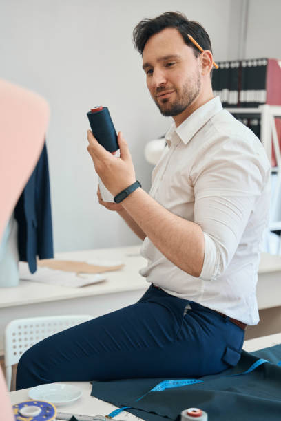 istock Man couturier examines black threads sitting on the desk 1407590486