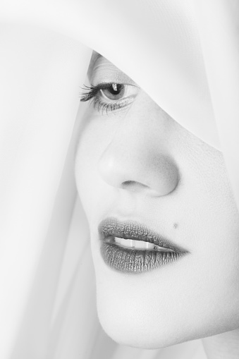beautiful young woman with eastern makeup cover her head with white veil looking aside closeup portrait, monochrome
