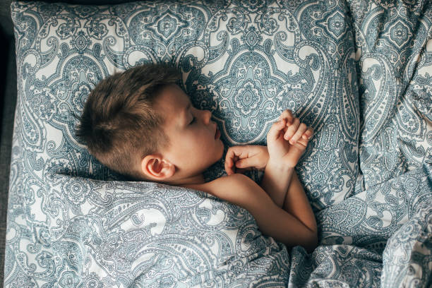 istock Cute boy sleeping in bed. Child 6-7 years old smiling, having a good dreams. 1407599252
