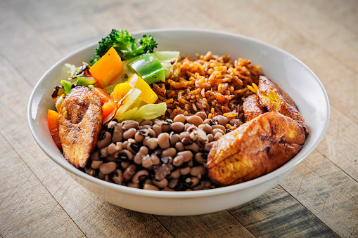 Vegan veggie bowl with jollof rice, steamed vegetables, black eyed peas stew, plantains.