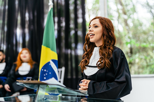 Portrait of confident young woman giving speech to microphone while sitting at table in conference room, copy space