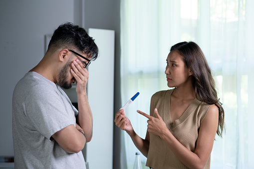 Depressed young  Asian woman feeling sad while looking at the positive results of a pregnancy test. Husband are not ready to have children, relationship problems concept