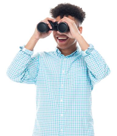 Waist up of aged 18-19 years old with curly hair generation z teenage boys standing in front of white background wearing pants who is laughing who is searching and holding binoculars