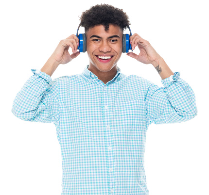 Front view of aged 18-19 years old with black hair generation z male standing in front of white background wearing button down shirt who is listening and using headphones
