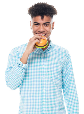 Waist up of aged 18-19 years old with black hair generation z teenage boys standing in front of white background wearing button down shirt who is hungry and holding sandwich