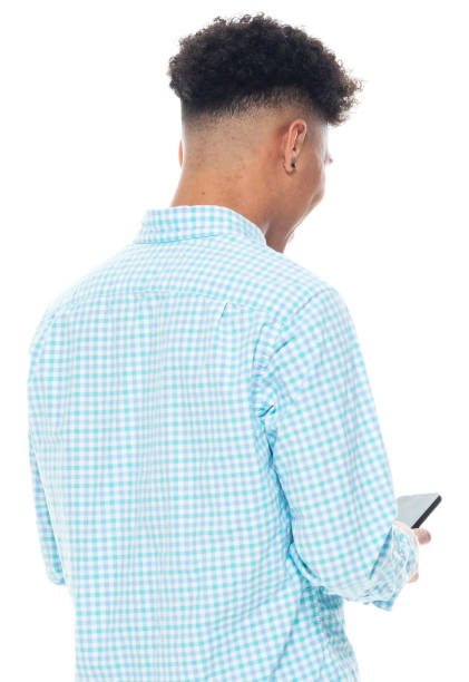 African-american ethnicity male standing in front of white background wearing button down shirt and using smart phone Portrait of aged 18-19 years old with black hair african-american ethnicity male standing in front of white background wearing button down shirt and using smart phone teenager boy haircuts stock pictures, royalty-free photos & images