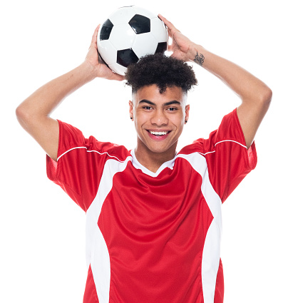 Portrait of aged 18-19 years old with black hair african-american ethnicity teenage boys athlete standing in front of white background wearing soccer uniform who is showing cool attitude and holding soccer ball and playing soccer - sport and using sports ball