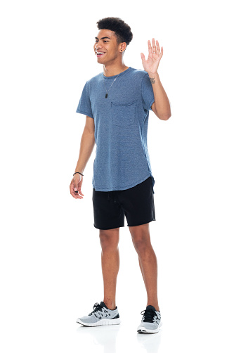 Side view of aged 18-19 years old with curly hair african-american ethnicity young male standing in front of white background wearing t-shirt who is laughing and greeting and showing high-five