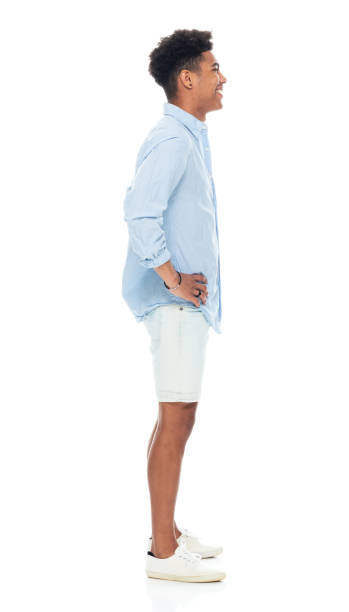 Generation z teenage boys standing in front of white background wearing canvas shoe Side view of aged 18-19 years old with black hair generation z teenage boys standing in front of white background wearing canvas shoe who is smiling with hand on hip man standing profile stock pictures, royalty-free photos & images