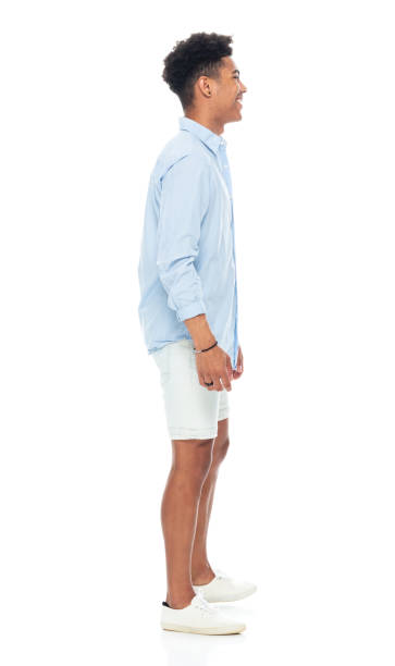 African-american ethnicity young male standing in front of white background wearing canvas shoe Side view of aged 18-19 years old with black hair african-american ethnicity young male standing in front of white background wearing canvas shoe who is smiling with hand by side man standing profile stock pictures, royalty-free photos & images