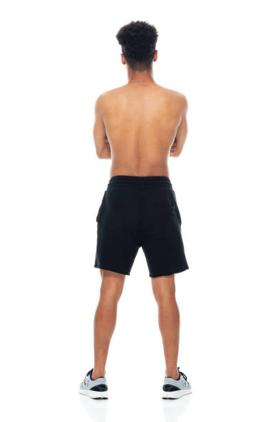 African-american ethnicity young male standing in front of white background wearing sports shoe Rear view of aged 18-19 years old with black hair african-american ethnicity young male standing in front of white background wearing sports shoe who is confident with arms crossed ass boy stock pictures, royalty-free photos & images