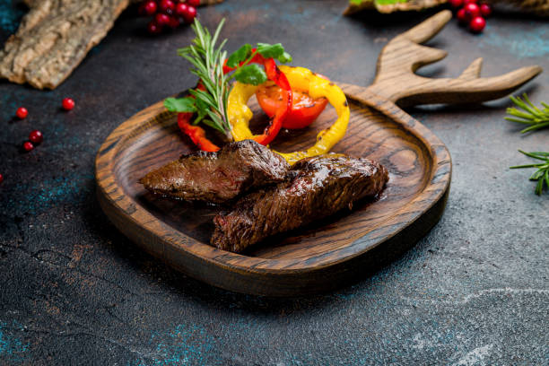 venison steak with sliced vegetables on the board on dark table - venison imagens e fotografias de stock