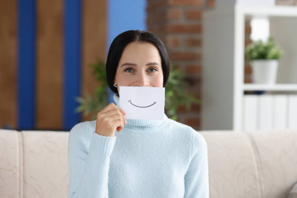 Woman holds painted smile for on piece of paper closeup Woman holds painted smile for on piece of paper. Positive emotions and mood concept cheesy grin stock pictures, royalty-free photos & images