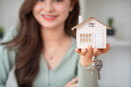 Woman holding white house model and house key in hand. Mortgage loan approval home loan and insurance concept.