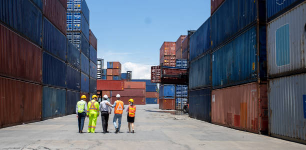 Group workers people in safety uniforms and hard hats work at logistics terminal with many stacks of containers ,Engineer dock worker wear safety uniform check control loading freight cargo container los trabajadores del grupo personas con uniformes de seguridad y cascos trabajan en la terminal logística con muchas pilas de contenedores, el ingeniero portuario usa uniforme de seguridad control de control de carga de carga de contenedores de carga