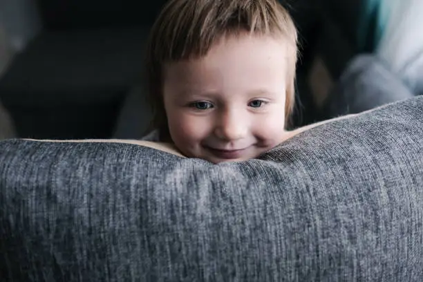 Photo of funny European child playing with pillows on couch