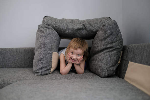 Kid Toddler builds house from pillows on sofa in living room, lifestyle and games in real interior