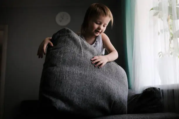 Photo of funny European child playing with pillows on couch