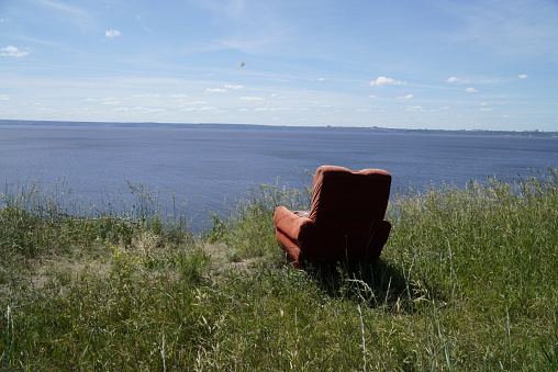 Picturesque Summer landscape with red old armchair on a high bank with a beautiful view of the Volga River. Ulyanovsk, Russia