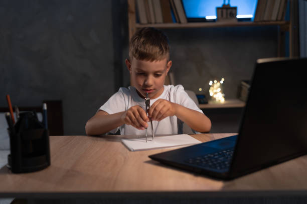 istock boy with drawing mathematic compass learning at home at night using laptop for online lesson 1407635385