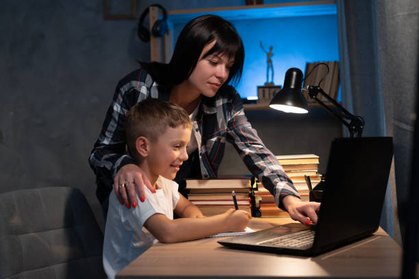 istock Young mother and son using laptop computer for study and learning together at home in evening, boy writing on notebook for homework, mom support child, home education 1407635558
