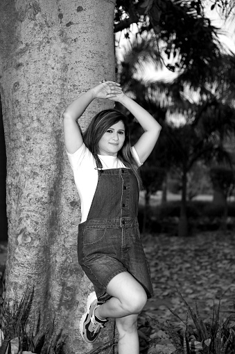 Full length image of mature Indian woman standing with tree trunk outdoors in park, Delhi, India.