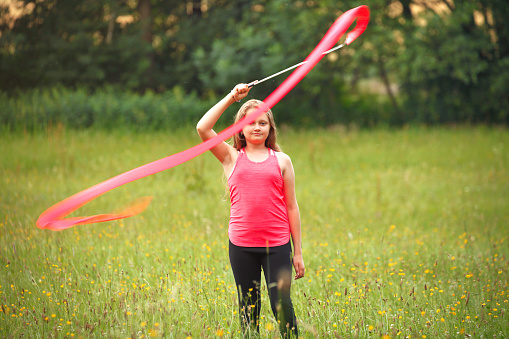Young girl exercising on the meadow with a ribbon
