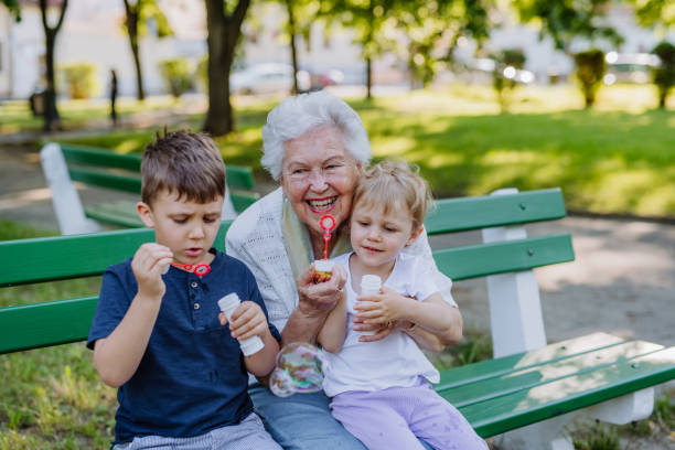 urgroßmutter sitzt mit ihren enkelkindern auf der bank und bläst seifenblasen zusammen, generationen-familienkonzept. - great grandmother stock-fotos und bilder