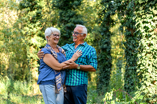 A senior Caucasian couple is cheerfully embracing each other, while taking a walk through the forest.