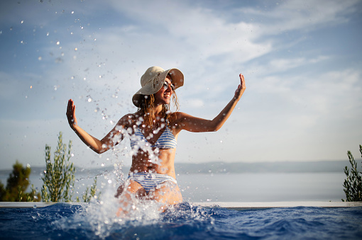 A young beautiful woman making water splash at the pool, enjoying summer. Summer vacation concept.