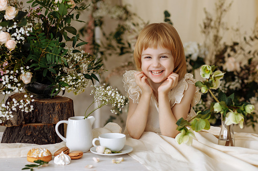 A girl in a vintage dress sits at a table at breakfast. Antique interior, white kemika, natural flowers.