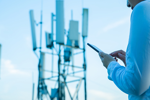 Human hand using mobile phone near 4G,5G communications tower