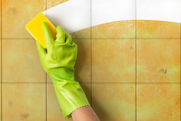 Hand cleaning a dirty ceramic tile wall with a sponge stock photo