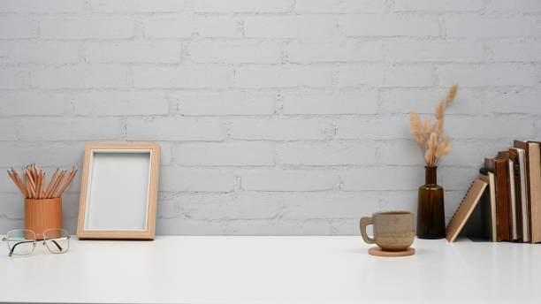 istock Creative workspace with picture frame, pencil holder, books and coffee cup on white table. 1407652825