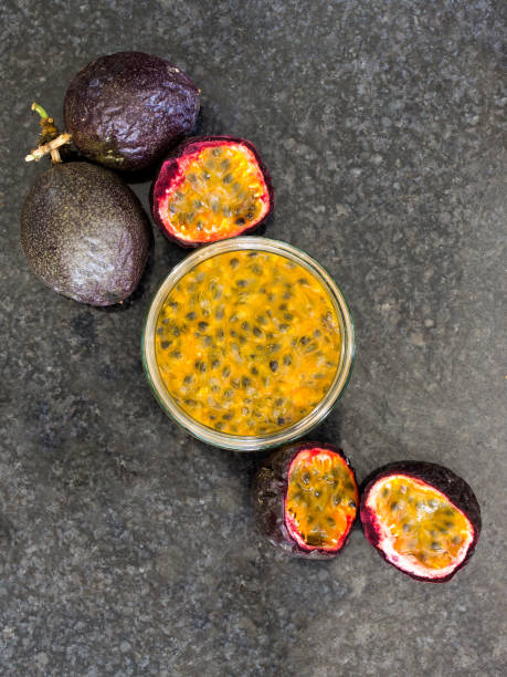 A bowl filled with passion fruit pulp, surrounded by whole and halved Passion Fruits stock photo