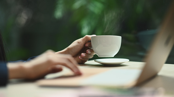 Cropped image of young woman hand holding cup of hot coffee with natural morning background.
