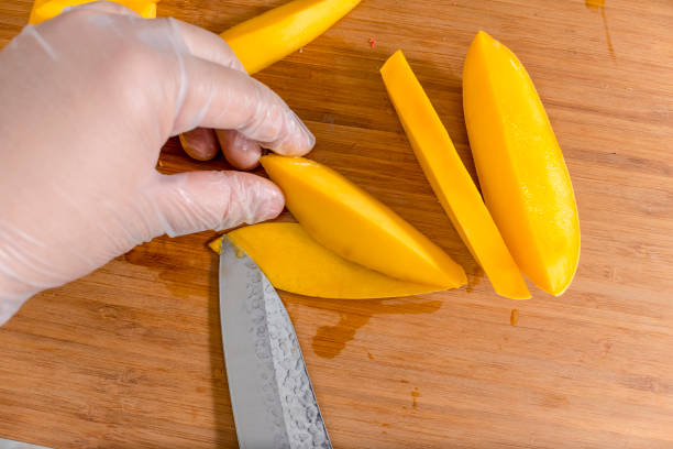 istock Removing the mango skin with a standard kitchen knife while wearing plastic gloves. Ingredient for California Maki. 1407657360
