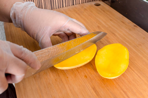 Slicing a ripe mango with a kitchen knife while wearing plastic gloves. Ingredient for California Maki.