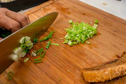 A cook chopping spring onions on a wooden board. With Lechon Carajay.
