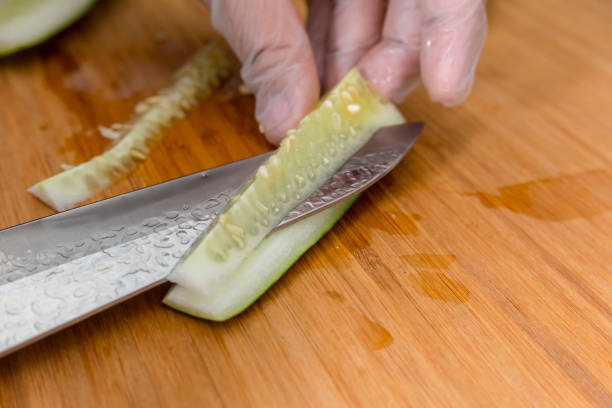 Removing the seed pit and core of a cucumber with a sharp stainless knife while wearing plastic gloves.