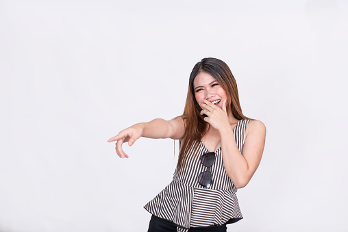 A young asian woman laughs and mocks someone while pointing with her finger. Isolated on a white background.